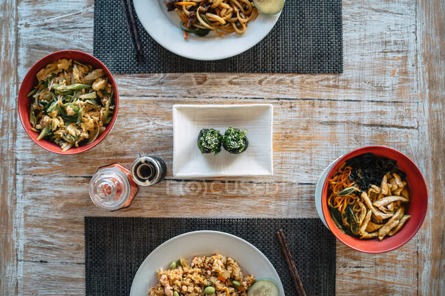Vista aerea di deliziosi involtini di sushi gunkan con chuka tra insalata di verdure e piatto di riso contro la salsa di soia sul tavolo — Foto stock