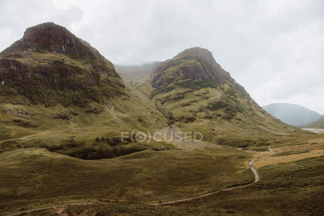 Dirt path on rough grassy hillside in Glencoe, UK countryside on cloudy day — Stock Photo