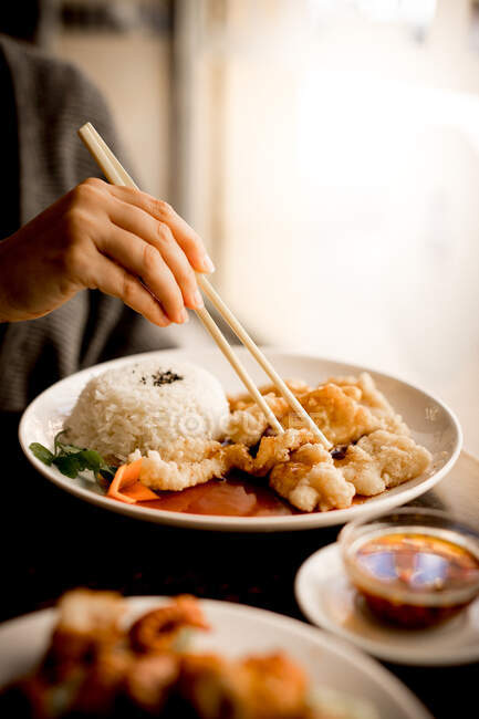Hand einer Frau, die am Tisch sitzt und mit Essstäbchen frittiertes chinesisches Fischmehl aus weißem Keramikteller isst — Stockfoto