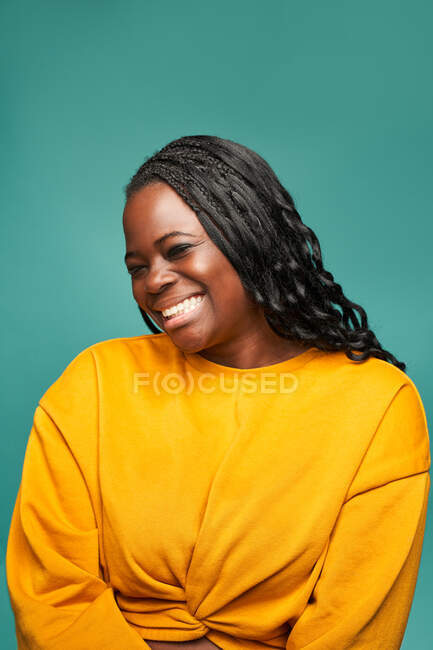 Glad African American female in yellow clothes with eyes closed standing against blue background — Stock Photo