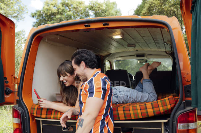 Délicieux couple de voyageurs assis dans un van et se prendre en photo sur smartphone tout en embrassant et en profitant de l'aventure estivale — Photo de stock