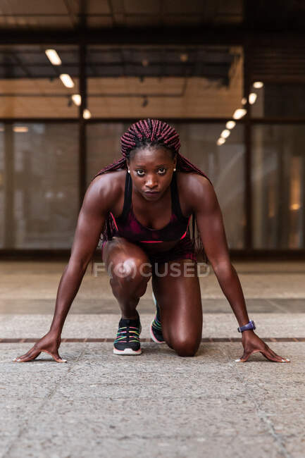 Femme sportive afro-américaine confiante debout sur le début accroupi préparé pour courir dans la rue — Photo de stock