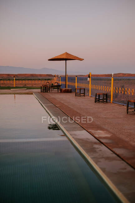 Stools and umbrella located on weathered poolside of hotel near desert during sunset in Marrakesh, Morocco — Stock Photo