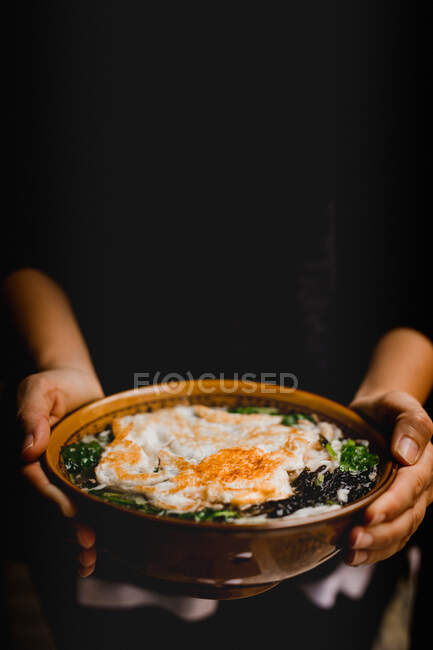Hands of anonymous person holding bowl of soup with noodles and egg — Stock Photo