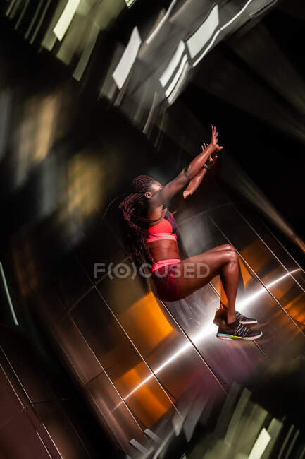 Ethnic sportswoman jumping on street at night — Stock Photo