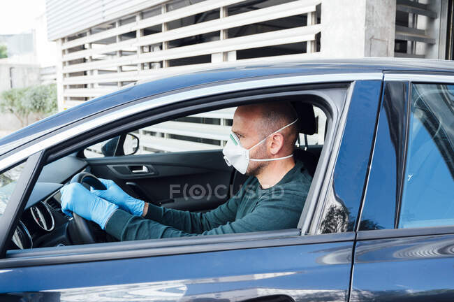 Vista lateral del hombre serio usando una máscara protectora que conduce el coche durante el tiempo de cuarentena - foto de stock