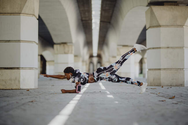 Молодая фитнес афроамериканка делает упражнения и слушает музыку после бега по городской улице — стоковое фото