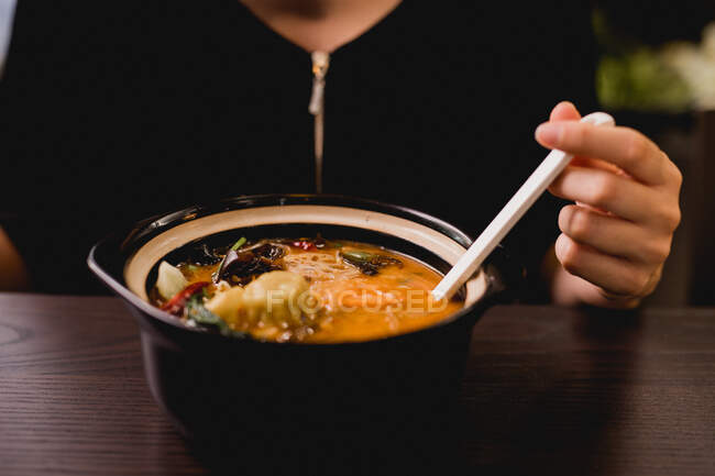 Рука жінки тримає ложку і їсть китайський суп з великої керамічної миски. — стокове фото