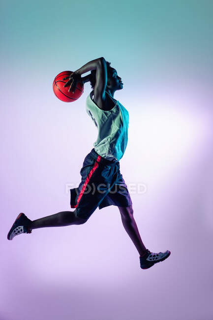 Черная женщина в баскетбольной форме в студии с помощью цветных гелей и прожекторов — стоковое фото