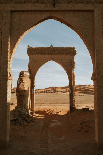 Арка разрушенного старого здания, расположенного в песчаной пустыне на фоне облачного неба в солнечный день недалеко от Марракеша, Морчо — стоковое фото