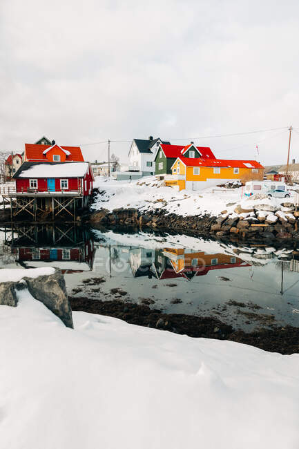 Banchina innevata in un tranquillo insediamento costiero con case rosse nella giornata invernale nuvolosa sulle isole Lofoten, Norvegia — Foto stock