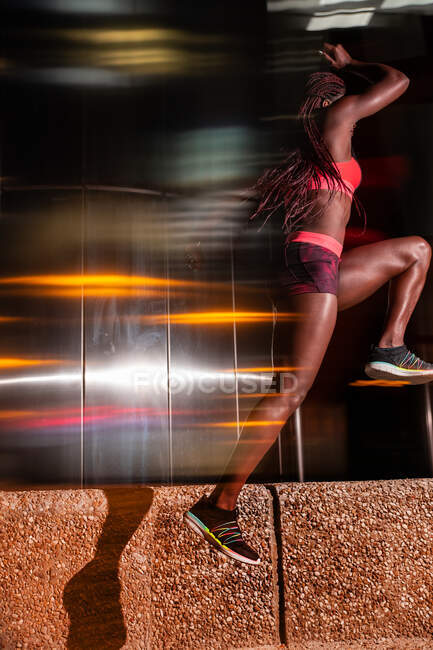 Ethnic sportswoman jumping on street at night — Stock Photo