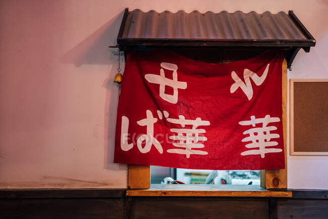 Tissu rouge avec hiéroglyphes asiatiques dans la fenêtre avec toit métallique du bâtiment moderne — Photo de stock