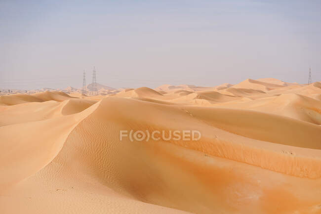 Paesaggio desertico minimalista con dune sabbiose e cielo azzurro negli Emirati. Torri di trasmissione a distanza. — Foto stock