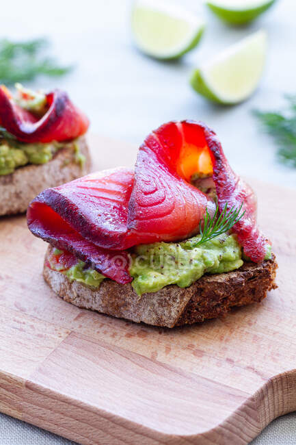 Gustosi antipasti di pane di segale tostato con diffusione di avocado e fette di salmone affumicato con rametti di aneto sul tagliere — Foto stock