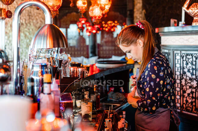 Focused female bartender garnishing fresh cocktails in glasses placed on counter in bar — Stock Photo
