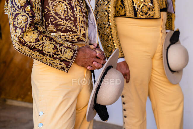 Crop anonymous picadors wearing traditional shiny costumes standing with hats and preparing for corrida festival — Stock Photo