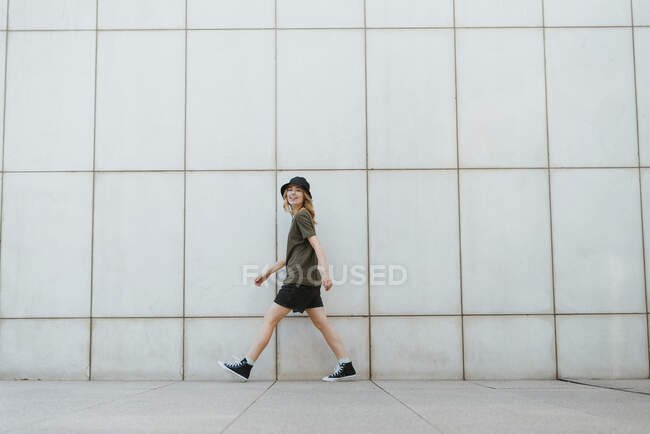 Vue latérale de la femme gaie en tenue décontractée et des chaussures de gomme marchant en regardant la caméra avec les bras tendus au-dessus de trottoir carrelé en ville — Photo de stock