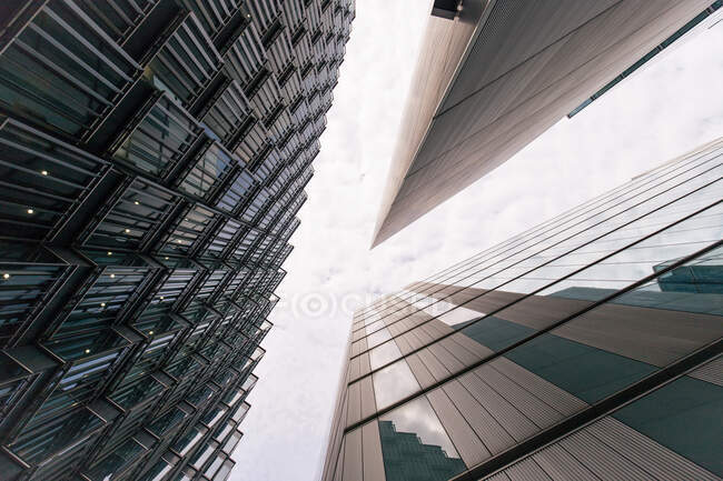 Desde abajo perspectiva de fachadas de rascacielos modernos con arquitectura exterior contemporánea bajo cielo nublado - foto de stock