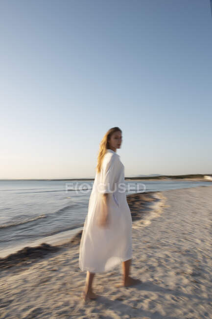 Mulher loira de cabelos compridos em pé na praia olhando para a distância — Fotografia de Stock