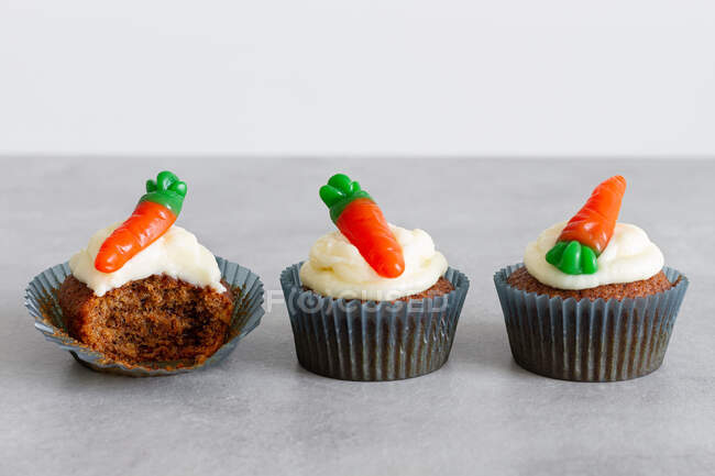 Fileiras de doces deliciosos cupcakes de cenoura com creme macio e gomas em forma de cenoura na superfície cinza — Fotografia de Stock