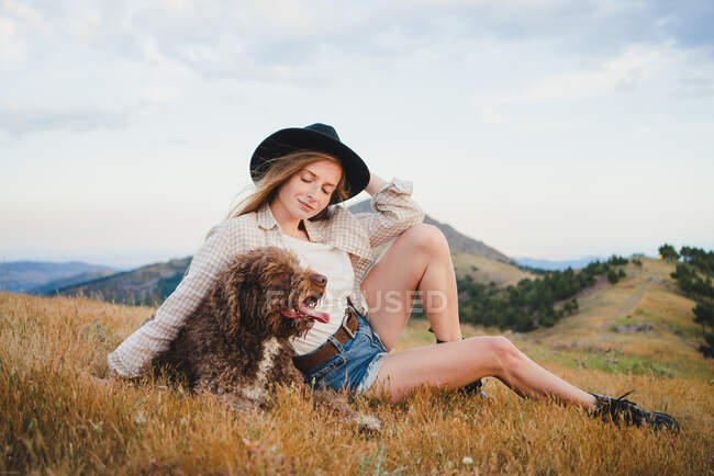 Female owner with obedient Labradoodle dog sitting in mountains looking away — Stock Photo