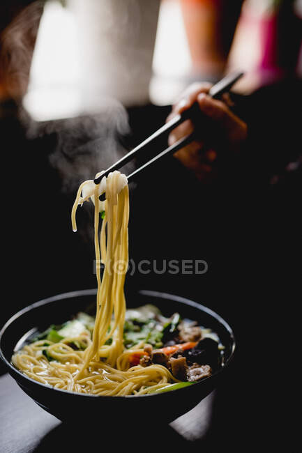 Hand einer unkenntlichen Frau, die im Café Nudeln mit Stäbchen aus einer Schüssel pikanter asiatischer Suppe pflückt — Stockfoto