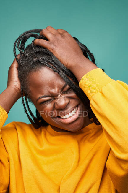 Glad African American female in yellow clothes with eyes closed touching head against blue background — Stock Photo