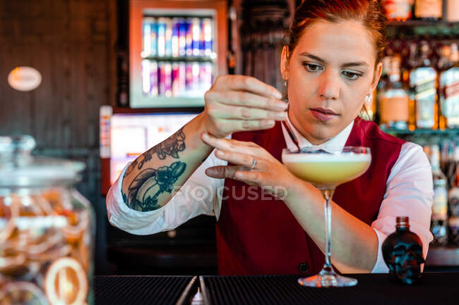 Професійна молода жінка бармен додає алкоголь з пляшки у формі черепа з крапельницею в склянку під час приготування кислих коктейлів у барі — стокове фото