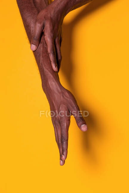 Recorte vista de hombre negro musculoso anónimo tocando su antebrazo con la mano sobre fondo amarillo - foto de stock