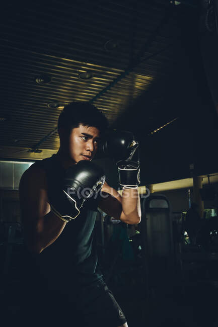 Jovem focado homem asiático treinamento boxe realizando socos durante o exercício com pesado saco de perfuração em um ginásio moderno — Fotografia de Stock