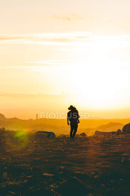 Вид ззаду анонімного чоловіка, який тримає дитину в повітрі в скелястій грубій долині на заході сонця — стокове фото