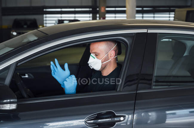 Visão lateral do homem sério usando uma máscara protetora colocando luvas de condução do carro durante o tempo de quarentena — Fotografia de Stock