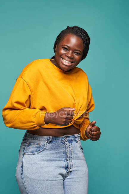 Веселий афроамериканець у модному жовтому одязі з радістю танцює на синьому фоні у студії. — стокове фото