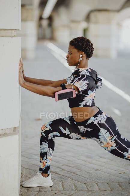 Joven fitness mujer afroamericana estirando las piernas antes de correr en la calle de la ciudad - foto de stock