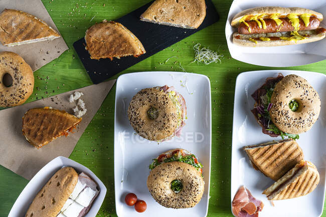De cima vários deliciosos sanduíches de bagel e cachorro-quente servido em fundo de mesa verde — Fotografia de Stock