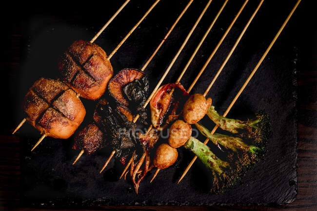 De dessus composition de brochettes grillées savoureuses avec viande, poisson, calmar et brocoli dans le café — Photo de stock