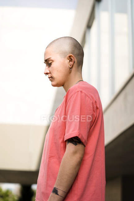 Side view of transgender person in t shirt standing looking down against masonry construction in daytime — Stock Photo