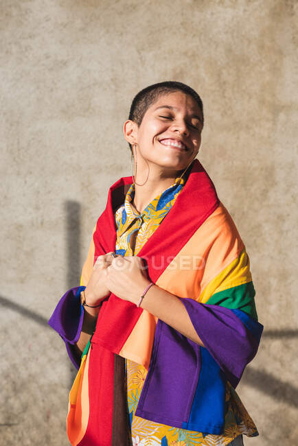 Contenu jeune femme bisexuelle ethnique aux yeux fermés et drapeau multicolore représentant les symboles LGBTQ le jour ensoleillé — Photo de stock