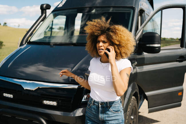 Besorgte junge Afroamerikanerin mit lockigem Haar telefoniert mit Handy und bittet nach Unfall mit Wohnmobil auf dem Land um Hilfe vom Reparaturdienst — Stockfoto