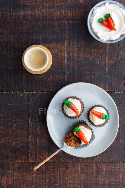 Vista superior da placa com deliciosos cupcakes vegetais com pequena cenoura decoração doce no topo colocado na mesa de madeira — Fotografia de Stock