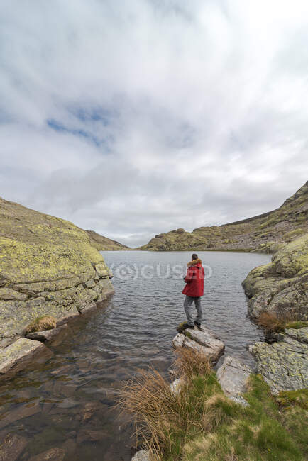 Vista laterale dell'uomo anonimo in capispalla in piedi su pietre vicino al lago Laguna Grande tra le montagne della Sierra de Gredos a Avila, Spagna — Foto stock