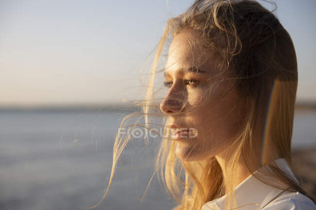 Довгошерста блондинка стоїть на пляжі, дивлячись на відстань — стокове фото