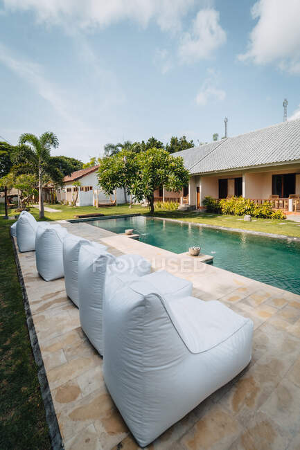 Row of loungers against rippled pool and house facade under cloudy sky on sunny day — Stock Photo