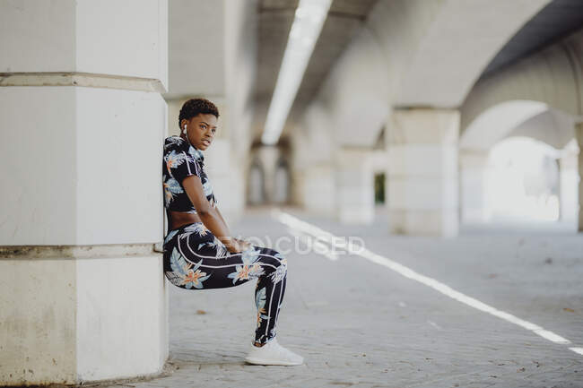 Young fitness African American woman resting and stretching legs after running on city street — Stock Photo