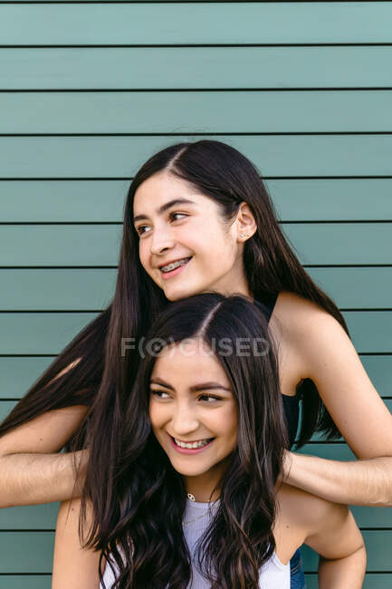 Aufrichtiger weiblicher Teenager lehnt mit den Händen auf dem Kopf von Geschwistern, während er tagsüber wegschaut — Stockfoto