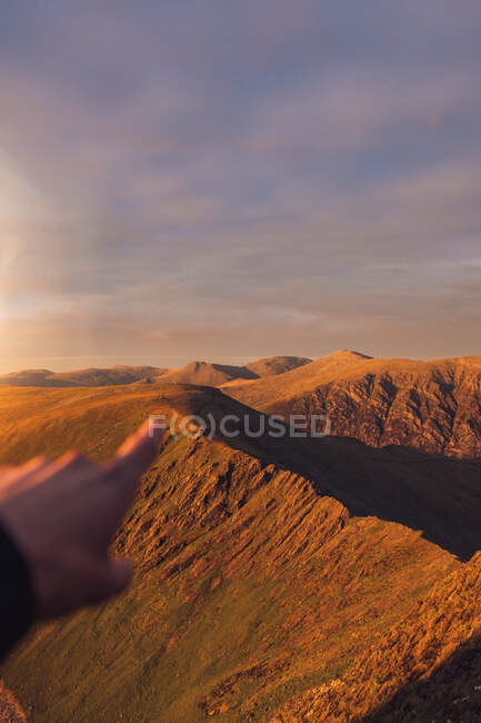 Vista de POV de un excursionista irreconocible apuntando hacia las tierras altas bajo el cielo al atardecer durante el trekking en Gales - foto de stock