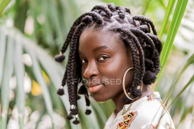 Stylish charming beautiful African American lady with African braids looking at camera in green park — Stock Photo