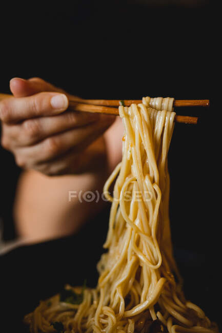 Mano de mujer sosteniendo palillos de bambú con sabrosos fideos de trigo de plato de harina de ramen chino - foto de stock