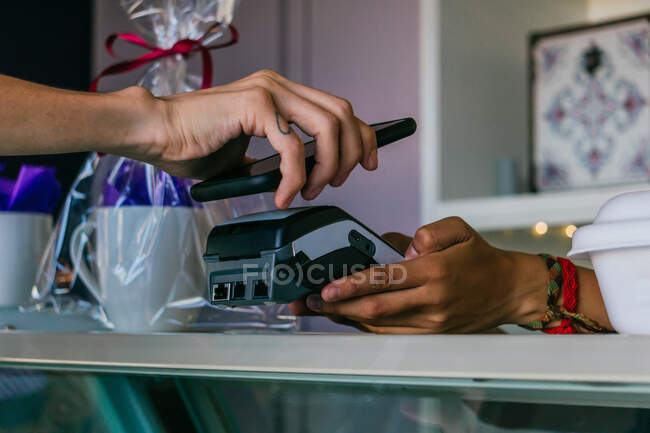 Crop anonymous customer making contactless payment on POS terminal with mobile phone in store — Stock Photo